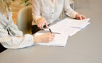 Två personer sitter vid ett bord och antecknar på papper