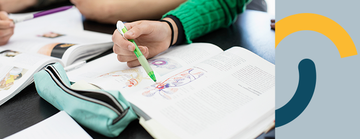 En lärobok, där en hand från en elev syns.