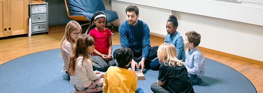 En grupp förskoleelever sitter på golvet med en lärare