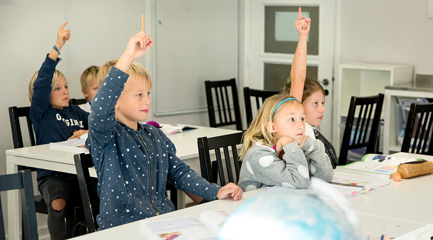 Elever sitter i klassrum och räcker upp handen