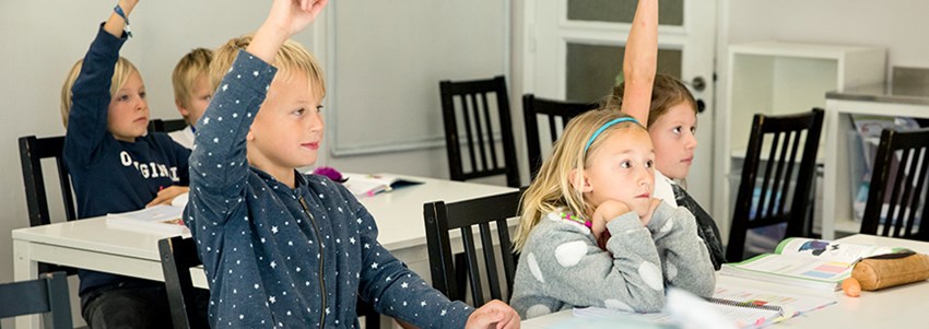Elever sitter i klassrum och räcker upp handen