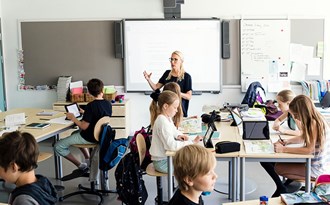 Fotat ovanifrån förklarar lärare för klass som sitter med iPads
