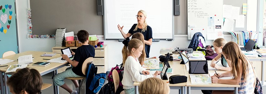 Fotat ovanifrån förklarar lärare för klass som sitter med iPads