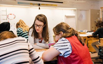 En lärare hjälper två mellanstadieelever i ett klassrum vid bänkarna