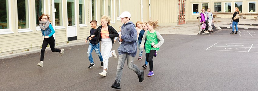Barn springer på en skolgård medan föräldrar tittat på