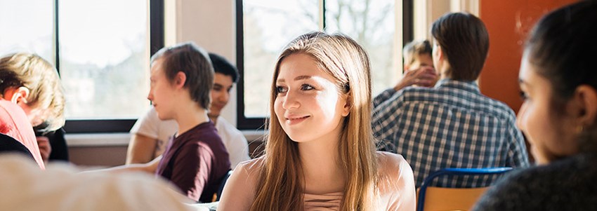 En gymnasieelev med klasskamrater sitter i ett klassrum och väntar