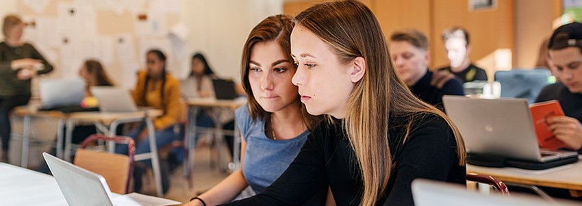 Gymnasieelever studerar med datorer under en lärarledd lektion