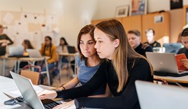 Gymnasieelever studerar med datorer under en lärarledd lektion