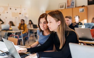 Gymnasieelever studerar med datorer under en lärarledd lektion