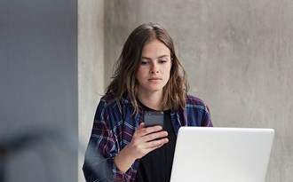 Gymnasieelev studerar själv vid dator och tittar på telefonen