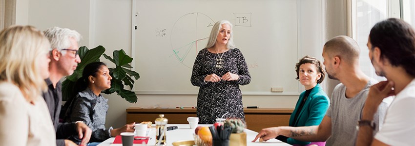 Rektor pratar inför en liten grupp kollegor som sitter runt ett bord