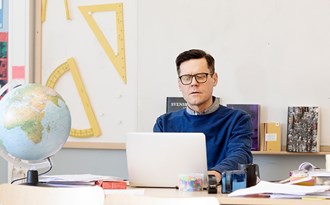 En lärare rättar prov på datorn vid katedern