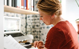 en vuxen kvinna läser en rapport framför datorn