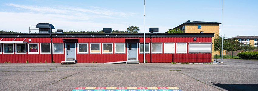 Skolbyggnad och skolgård under klarblå himmel