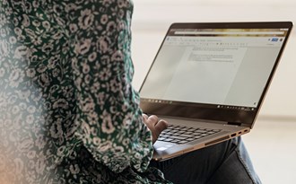 En person som skriver på en laptop som ligger på personens knän